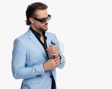 Photo for Portrait of handsome young man with sunglasses touching hands and looking to side in front of white background - Royalty Free Image