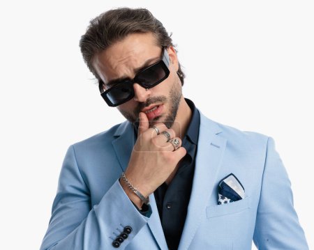 Téléchargez les photos : Séduisant jeune homme d'affaires avec des lunettes de soleil sensuellement toucher les lèvres devant fond blanc - en image libre de droit