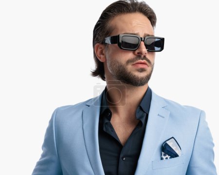 Foto de Retrato de hombre de negocios de moda sexy con gafas de sol mirando hacia otro lado y posando frente al fondo blanco - Imagen libre de derechos