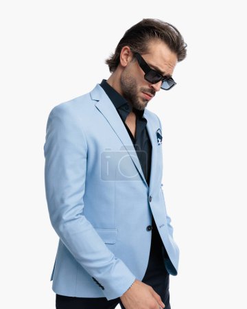 Téléchargez les photos : Portrait de mode cool homme d'affaires avec des lunettes de soleil regardant vers le bas et posant devant fond blanc - en image libre de droit
