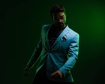 Téléchargez les photos : Homme d'affaires confiant avec des lunettes tenant les bras dans la pose de mode devant fond noir avec des lumières vertes - en image libre de droit