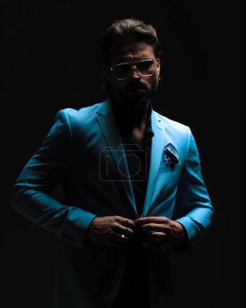 Téléchargez les photos : Homme de mode cool avec chemise défait regardant vers l'avant et costume d'ajustement en face de fond noir - en image libre de droit