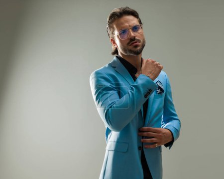 Téléchargez les photos : Élégant homme d'affaires avec des lunettes ajustement costume et regarder loin devant fond gris - en image libre de droit
