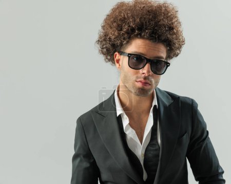Téléchargez les photos : Portrait d'un bel homme élégant avec des lunettes de soleil regardant vers l'avant et posant devant un fond gris - en image libre de droit