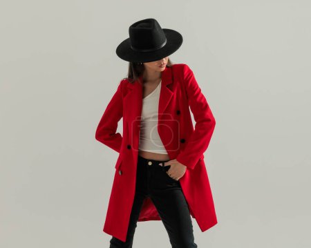 Foto de Sexy chica casual con sombrero y abrigo rojo de la mano en el bolsillo y mirando hacia abajo lado - Imagen libre de derechos
