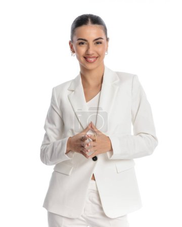 Téléchargez les photos : Confiant jeune femme d'affaires en costume blanc touchant les mains et souriant d'une manière fière devant fond blanc - en image libre de droit