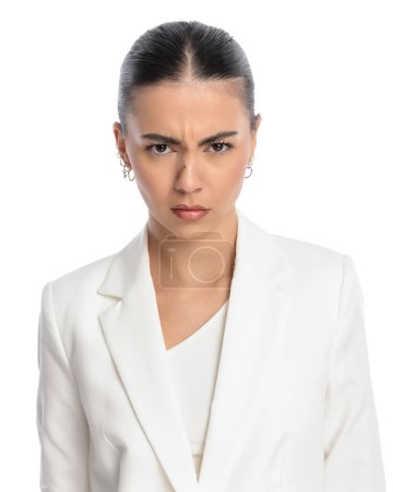 Photo for Portrait of upset young lady in white suit frowning while looking forward in front of white background - Royalty Free Image