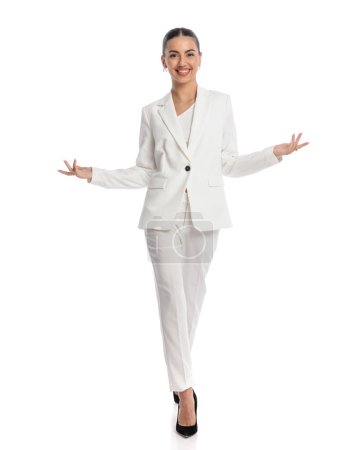 Photo for Confident elegant woman in white suit opening arms, walking and showing in front of white background - Royalty Free Image