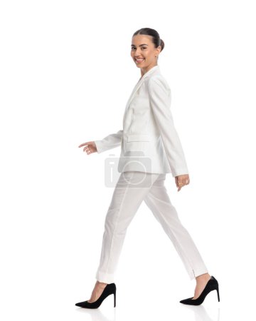 Téléchargez les photos : Image complète du corps de heureuse élégante jeune femme en costume blanc marche et être heureux devant fond blanc - en image libre de droit