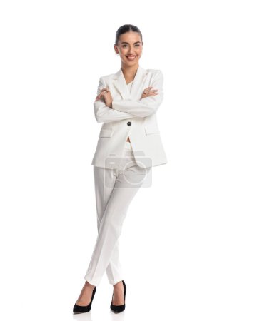 Photo for Full body picture of elegant businesswoman in white suit with black stiletto heels and bun hair folding arms and smiling on white background - Royalty Free Image