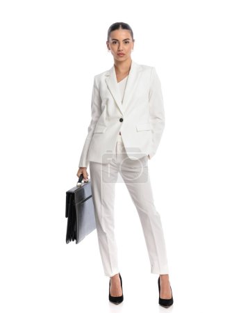 Téléchargez les photos : Sexy confiante femme en costume blanc tenant le sac et debout avec la main dans la poche devant fond blanc - en image libre de droit