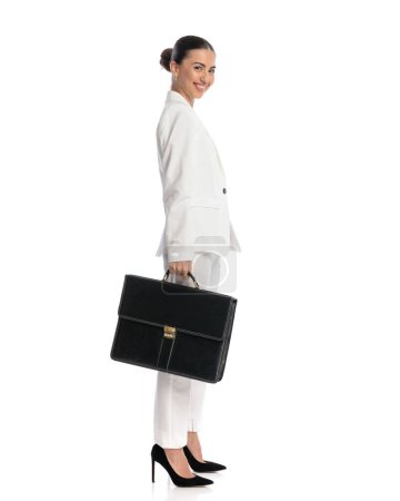 Photo for Full body picture of attractive elegant woman in white suit holding case and smiling in front of white background - Royalty Free Image