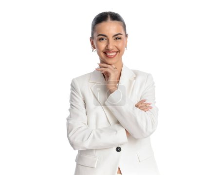 Téléchargez les photos : Portrait de heureuse femme élégante en costume blanc bras croisés et souriant devant fond blanc en studio - en image libre de droit
