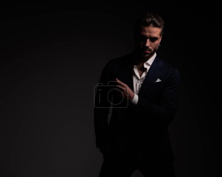 Photo for Mysterious young man in suit with open collar shirt holding hand in pocket in front of dark grey background - Royalty Free Image