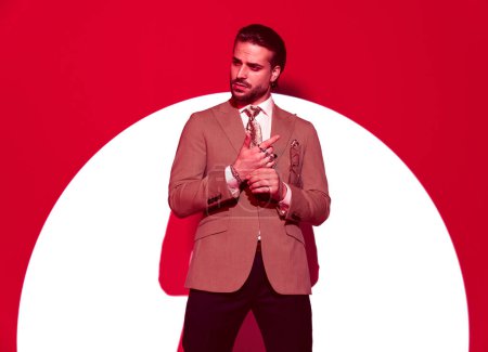 Foto de Retrato de hombre de negocios de alta clase en traje mirando a un lado mientras toca los dedos delante del centro de atención sobre el fondo rojo - Imagen libre de derechos