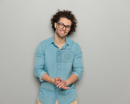 Foto de Retrato de joven guapo con gafas sonriendo y frotando las palmas delante de fondo gris - Imagen libre de derechos