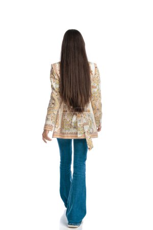Téléchargez les photos : Vue arrière de la jeune femme aux cheveux longs marchant devant fond blanc - en image libre de droit