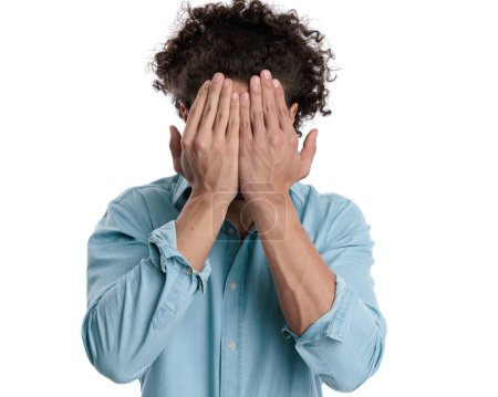 Photo for Closeup of unhappy casual man wearing blue shirt covering his face on isolated background - Royalty Free Image