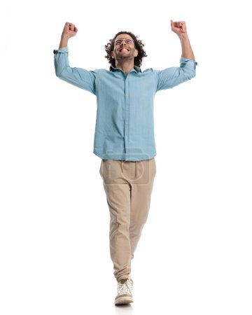 Photo for Celebrating casual man with hands in the air looking up while stepping forward on white background - Royalty Free Image
