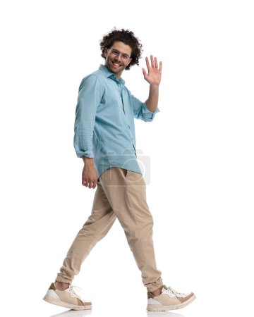 Photo for Happy casual man walking to side and making welcoming hand gesture on white background - Royalty Free Image