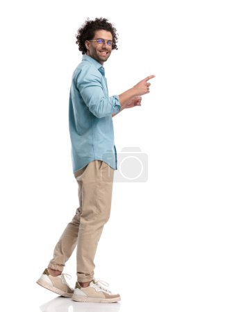 Photo for Side view of casual man pointing forward with his finger on white background - Royalty Free Image