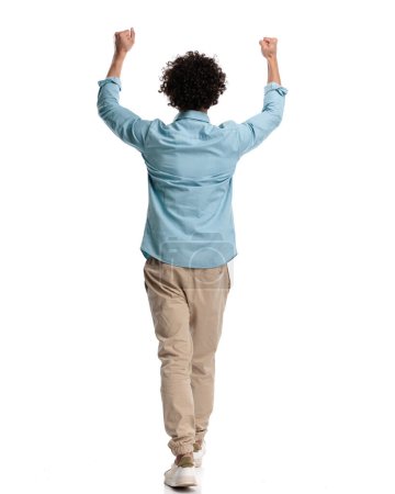 Foto de Vista trasera del joven hombre casual con el pelo largo y rizado sosteniendo puños en el aire mientras camina sobre un fondo de estudio aislado - Imagen libre de derechos