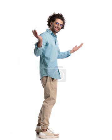 Photo for Side view of casual man making welcoming gesture and smiling while standing on white background - Royalty Free Image