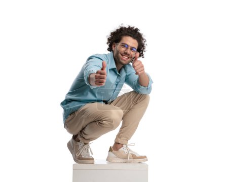 Photo for Joyful casual man leaning down on box making thumbs up sign while standing on isolated background - Royalty Free Image