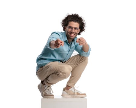 Photo for Casual man standing on box to fit the camera and pointing fingers on white background - Royalty Free Image