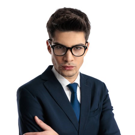 Photo for Portrait of serious elegant man with eyeglasses in suit crossing arms and looking forward in an intimidating way in front of white background - Royalty Free Image