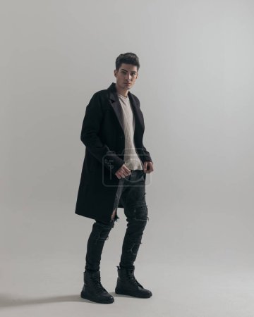 Photo for Side view of handsome young man wearing black overcoat while standing on white background, full body picture - Royalty Free Image