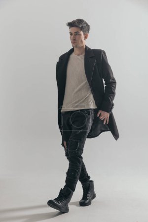 Foto de Atractivo joven con abrigo negro caminando a un lado sobre fondo gris - Imagen libre de derechos