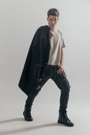 Photo for Confident young man holding black overcoat on shoulders stepping to side on gray background - Royalty Free Image