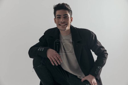 Photo for Closeup of sexy young man wearing black overcoat leaning down and laughing on gray background - Royalty Free Image