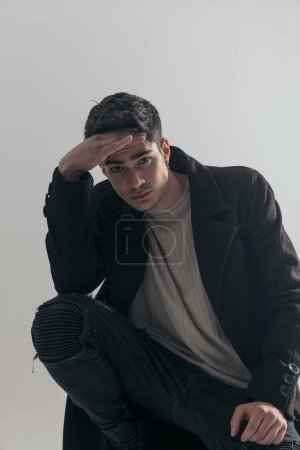 Photo for Closeup of handsome young man wearing black overcoat thinking while leaning down on white background - Royalty Free Image