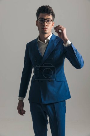 Foto de Chico de moda fresco en traje azul triple pecho con camisa de cuello abierto posando de una manera segura delante de fondo gris - Imagen libre de derechos