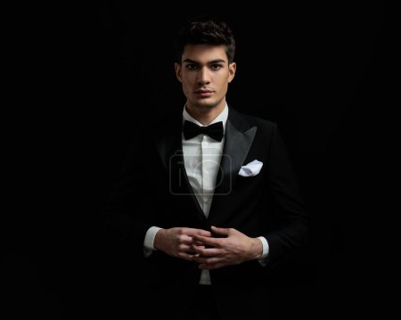 Foto de Retrato de novio atractivo con esmoquin negro y corbata de pie sobre fondo negro - Imagen libre de derechos