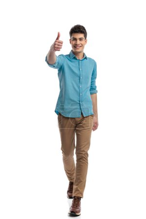 Photo for Young casual man in blue shirt making thumbs up sign while moving forward on white background - Royalty Free Image