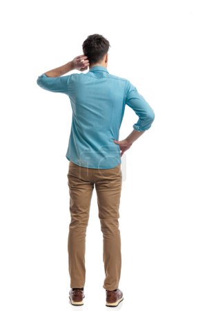 Photo for Back view of puzzled casual man scratching his head while holding his hip and standing on white background - Royalty Free Image