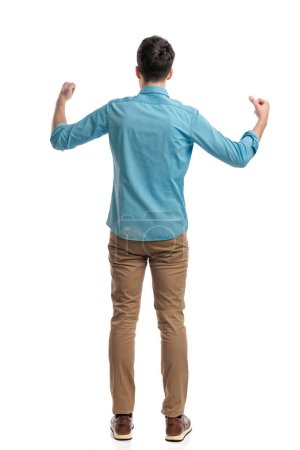 vista trasera del joven hombre casual celebrando con los puños en el aire mientras está de pie sobre fondo blanco