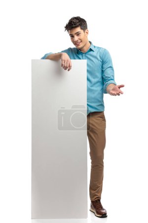 Photo for Young casual man wearing blue shirt and jeans is holding white board and presenting while standing on white background - Royalty Free Image
