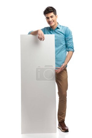 Photo for Attractive casual man presenting empty white ad while standing on white background and smiling - Royalty Free Image