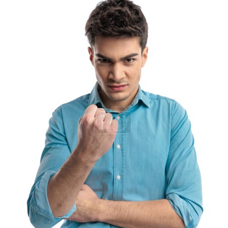 portrait d'un homme décontracté en colère portant une chemise bleue montrant son poing et menaçant sur fond blanc
