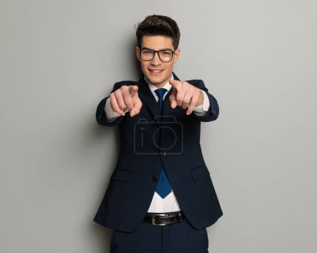 Foto de Retrato de joven empresario atractivo señalando los dedos mientras sonríe y de pie sobre fondo gris - Imagen libre de derechos