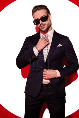 Foto de Sexy barbudo hombre de negocios con gafas de sol en traje de ajuste de corbata y posando de una manera fresca en frente de foco - Imagen libre de derechos