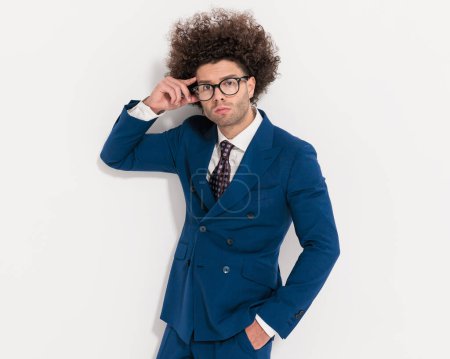 Foto de Sexy hombre de negocios con el pelo rizado de la mano en los bolsillos y gafas de fijación en frente de fondo gris - Imagen libre de derechos