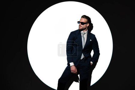 Foto de Sexy barbudo hombre de negocios en traje mirando a un lado y sosteniendo la mano en el bolsillo delante del centro de atención - Imagen libre de derechos