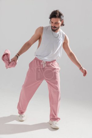 Foto de Cool fashion man con cuerpo en forma y brazos musculares caminando y posando de una manera segura frente al fondo gris - Imagen libre de derechos