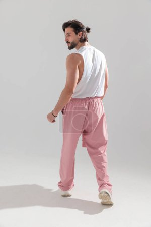 Foto de Vista trasera de hombre en forma sexy con ropa de gimnasio y mirando a un lado mientras camina de manera segura delante de fondo gris - Imagen libre de derechos