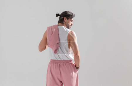 Photo for Behind view of muscular fit guy with hair tail holding hand in pocket while looking to side in front of grey background - Royalty Free Image